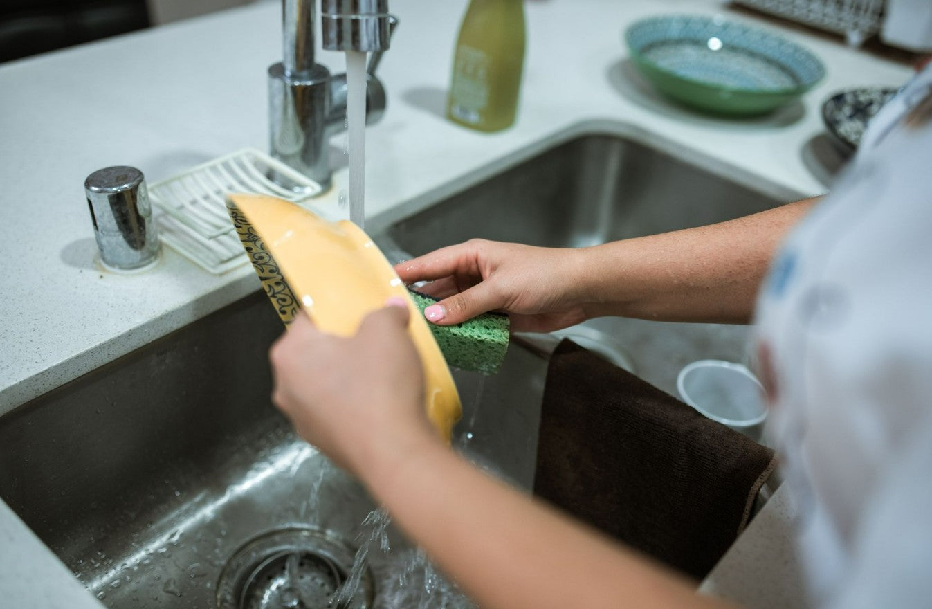Person scrubbing a yellow bowl with a green sponge at the kitchen sink